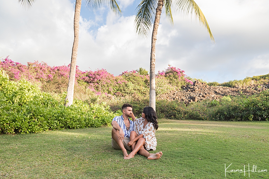 couple sitting on grass with tropical palm trees and flowers 