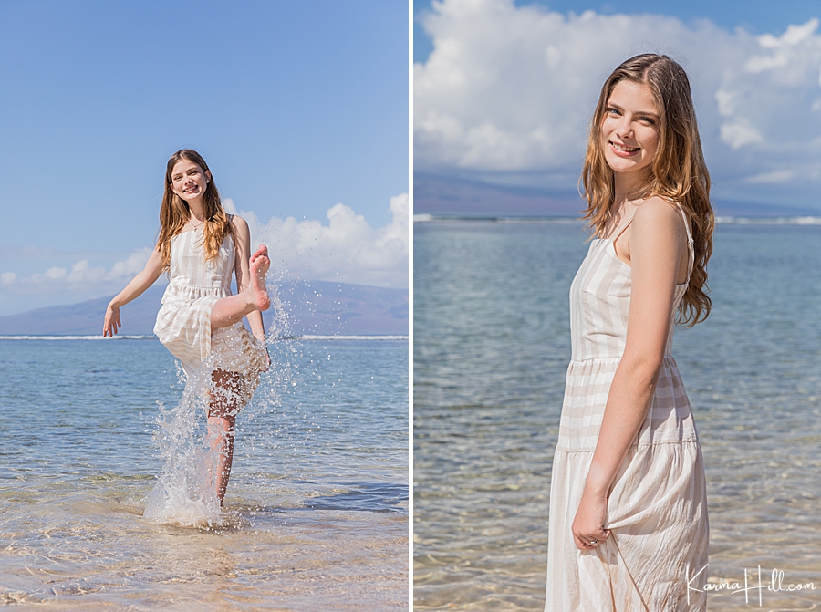 young woman in white stripped dress kicks in the ocean water in maui 