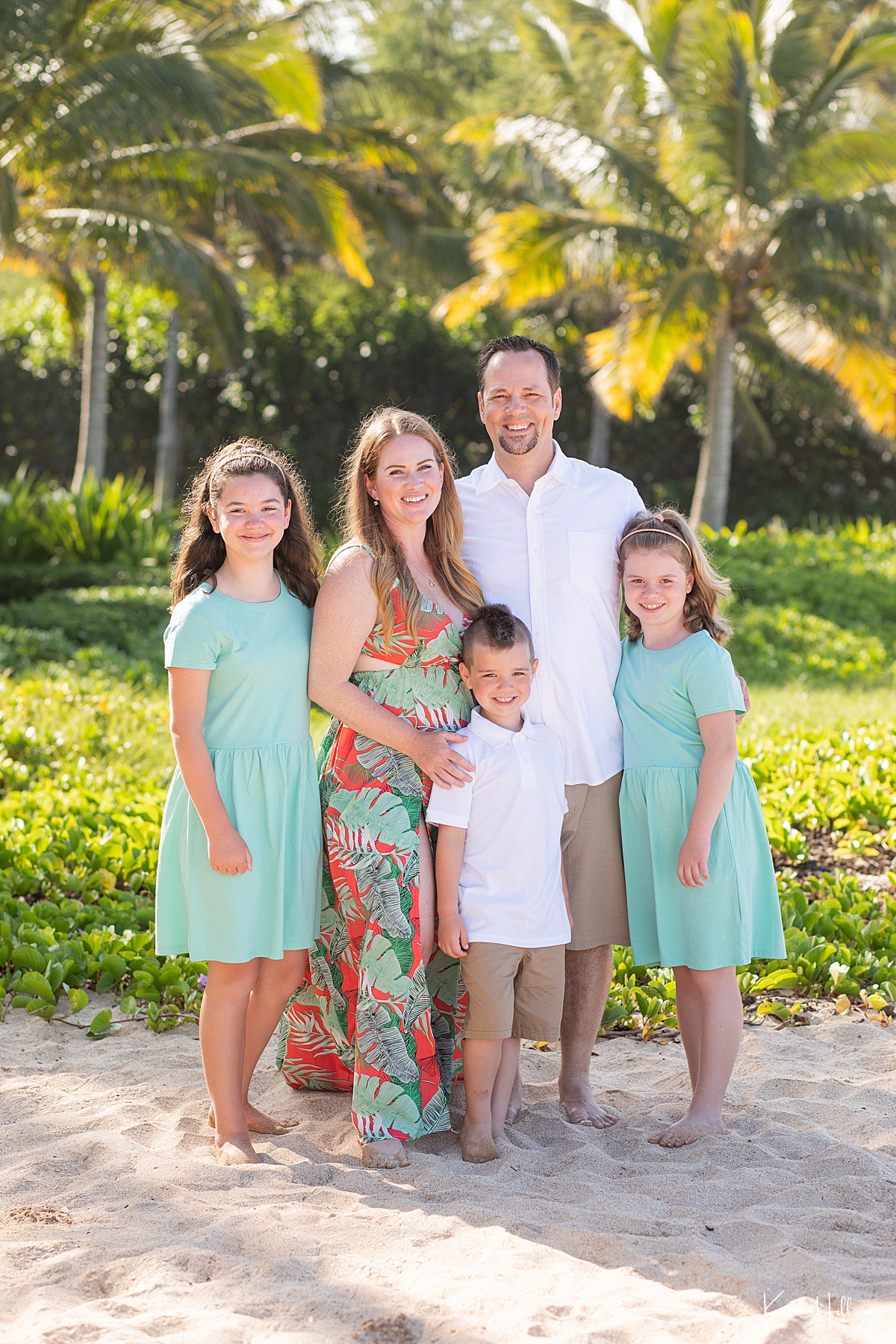 family of five wearing aqua and orange pose for a photo in front of maui palm trees