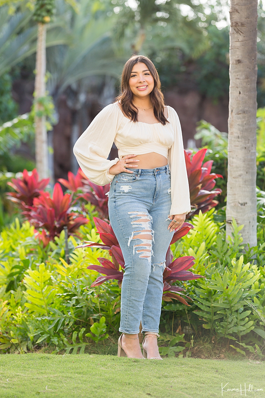 young woman stands in a tropical hawaiian lawn wearing a white crop top and jeans 