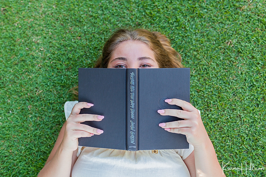 girl lying on grass with a john green book over her face 