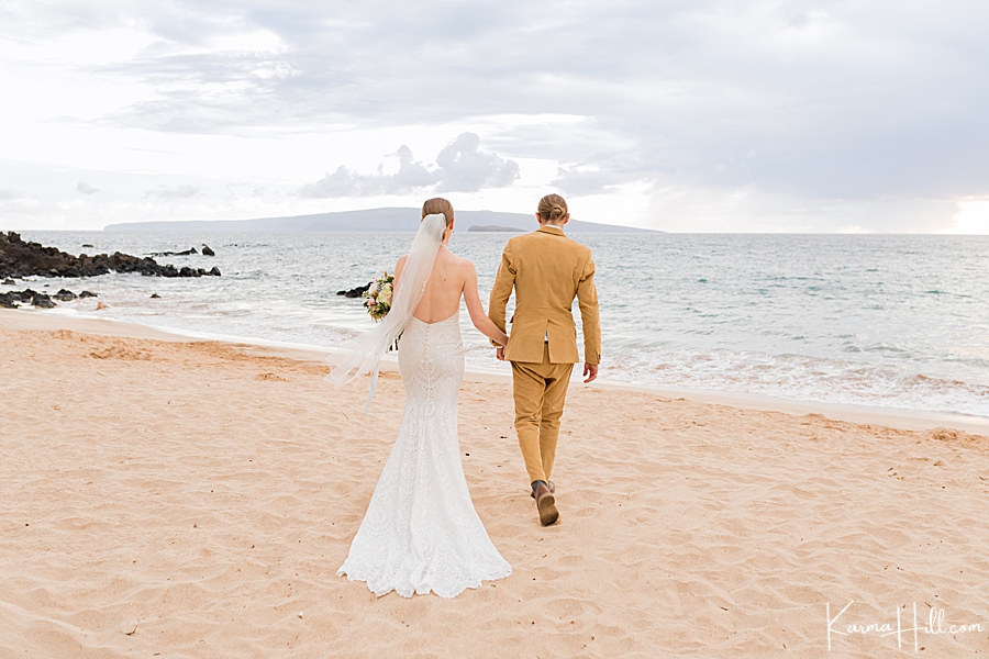 bride and groom walking away from the camera and holding hands on a beach in hawaii 