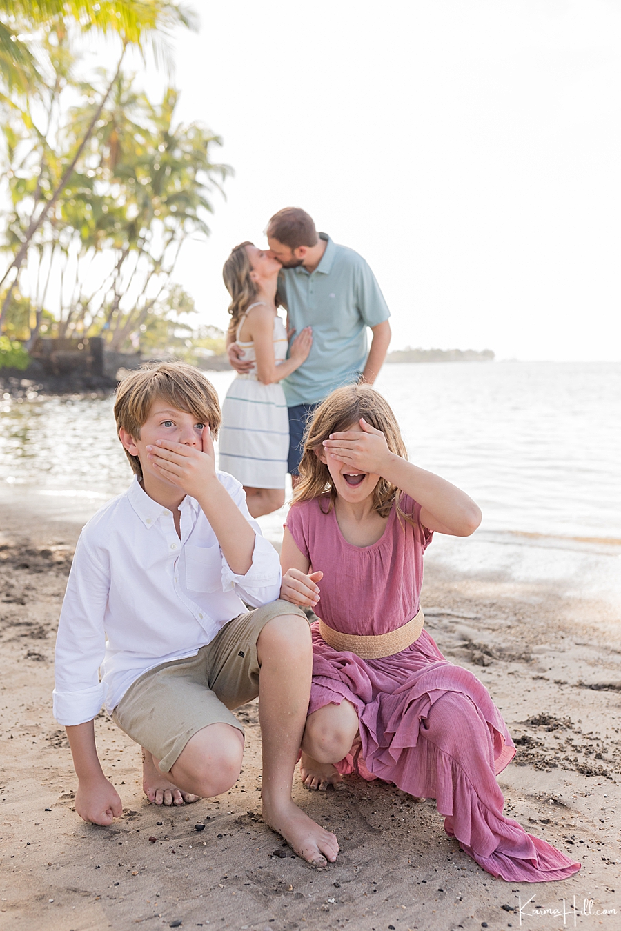 children cover eyes and mouth as parents kiss on Maui beach 