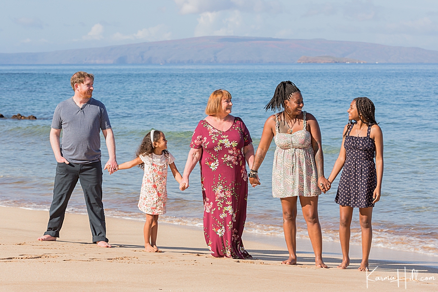 a blended family of five holds hands on maui shore 