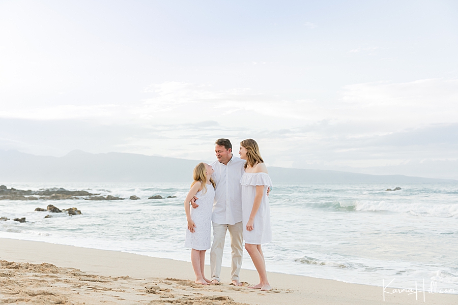 father and daughters stand on a maui beach dressed in all white 