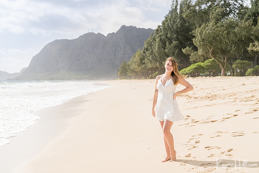 high school senior stands on the shore of Waimanalo wearing a white beach dress 