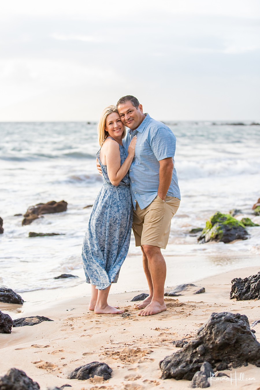 man and woman wearing shades of blue embrace in front of maui ocean 