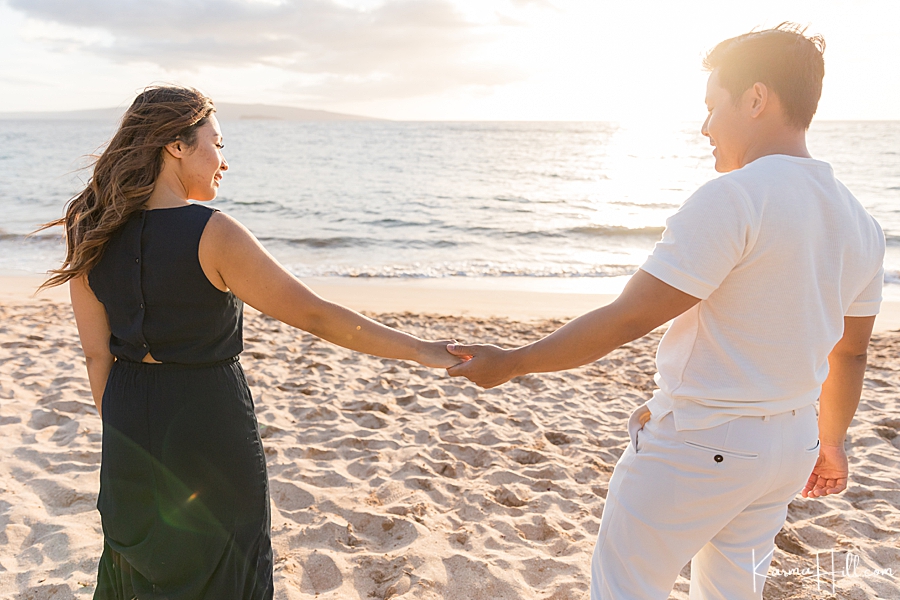 man and woman hold hands in front of a hawaii sunset on the beach 