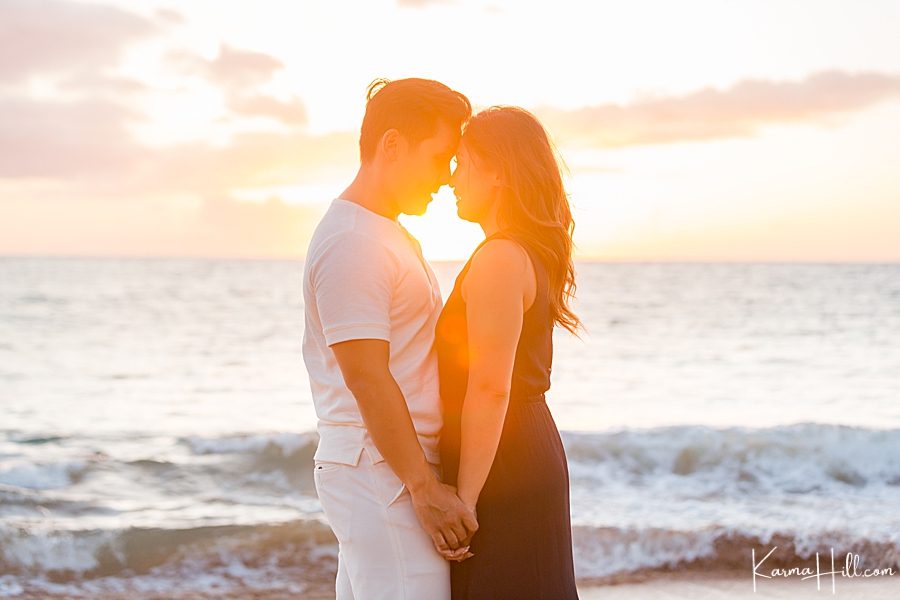man and woman touch foreheads in front of an orange hawaii sunset 
