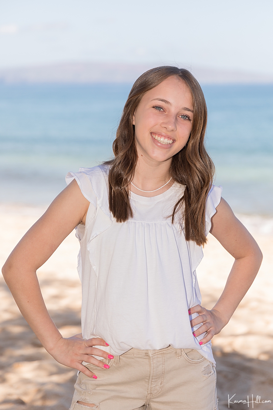 young girl with brown hair and blue eyes poses in front of the ocean 