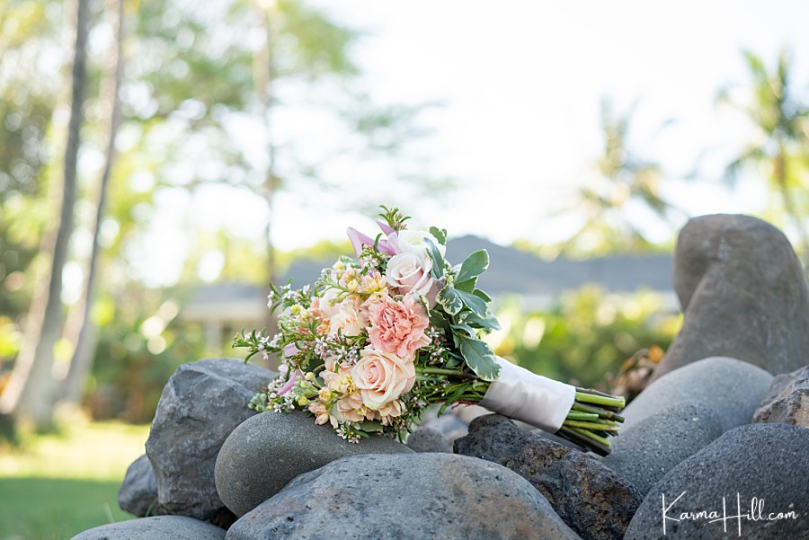 wedding bouquet of greenery roses and peonies resting on rocks with palm trees in the background 