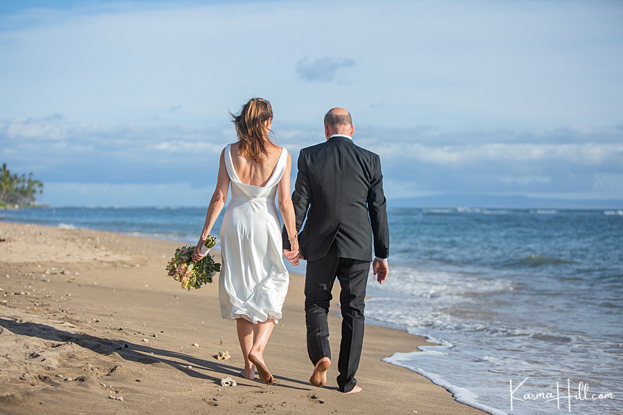 older couple walk hand in hand down a hawaii beach after their wedding 