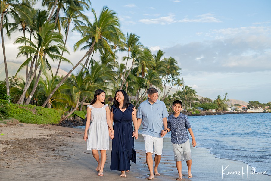 family of four hold hands and walk down a beach in lahaina  