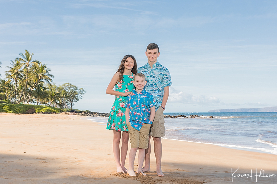 three children stand together wearing blue aloha print on maui beach 