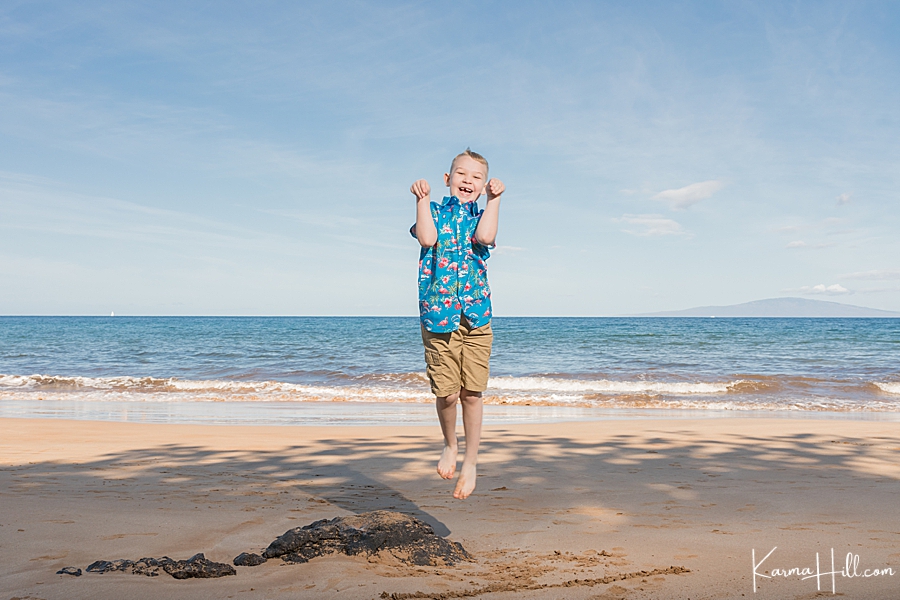 cute young boy jumps on the sand of a beach in hawaii 