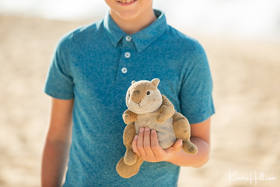 young boy holds a childhood stuffed animal while standing on maui beach 