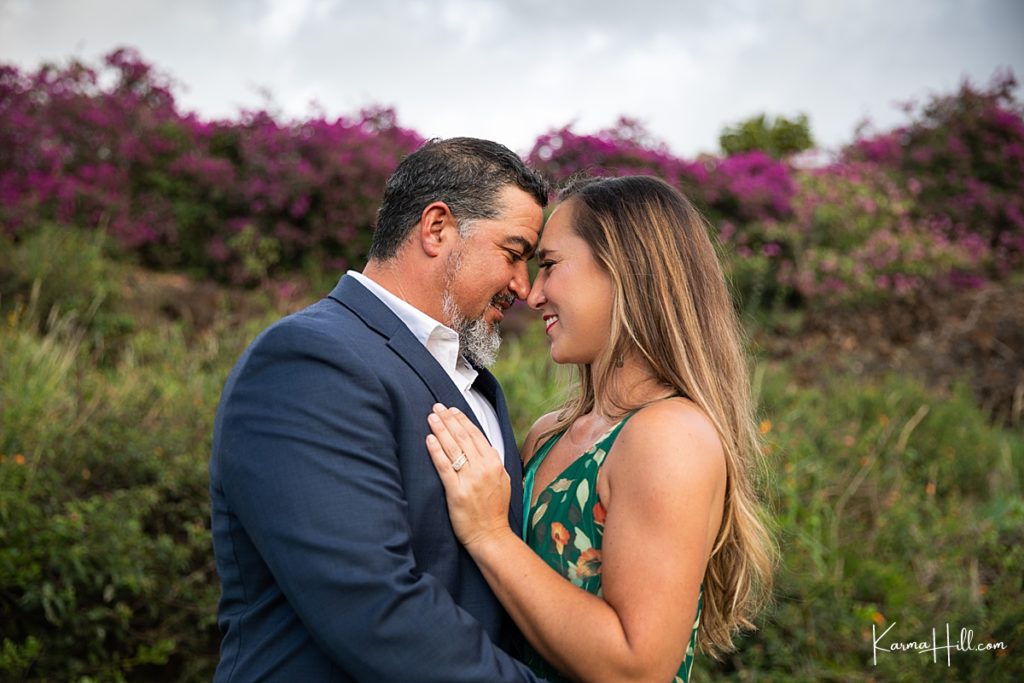 husband and wife touch foreheads with fuchsia flowers in the background 