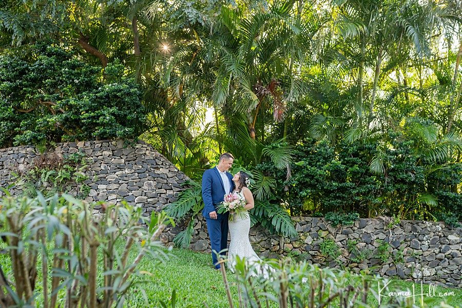bride and groom pose in front of a jungle and rock wall before their hawaii wedding 