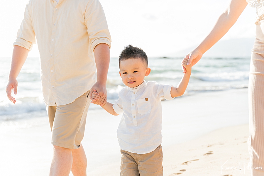 cute family photo with a little boy holding parents hands on maui beach 