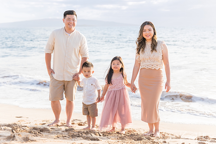 sweet family of four pose in nice clothes on hawaii beach while holding hands 