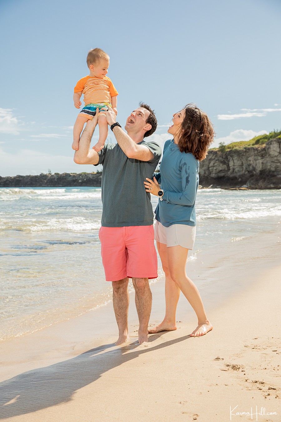 cute family with toddler son lift their son into the air on a beach in hawaii 