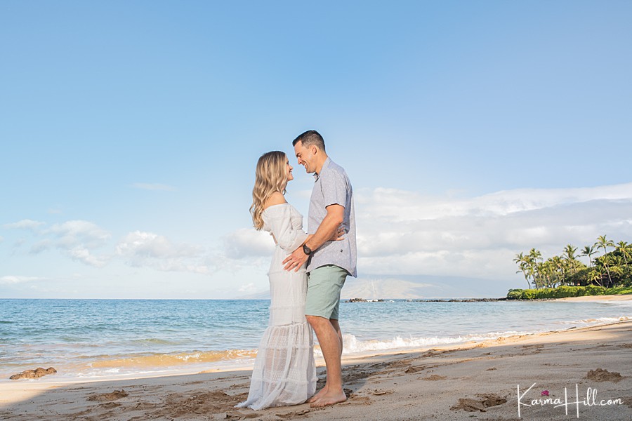 husband and wife hold each other and smile during their maternity photos in hawaii 