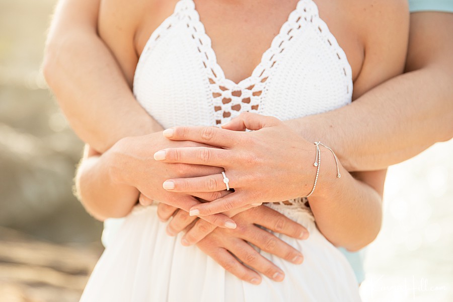 close up of couple's hands and they embrace highlighting woman's engagement ring 