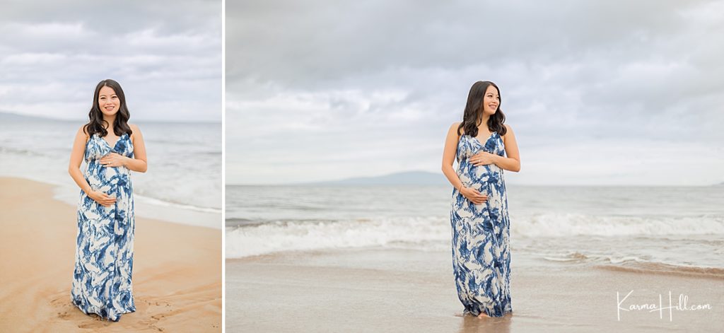 pregnant woman stands on the shore with the ocean in the background 