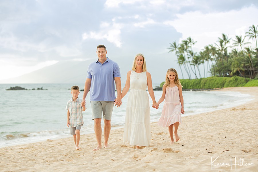 family of four wearing pastels stands on maui beach with palm trees in the background 