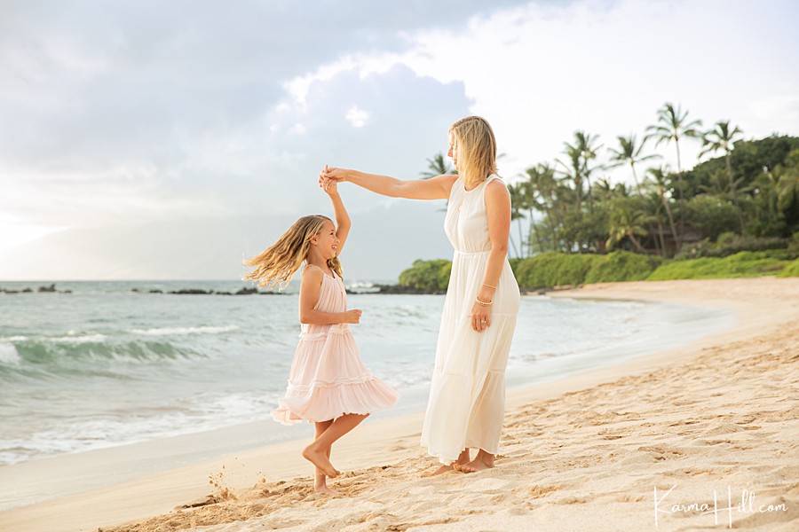 little girl in pink dress twirls with mom on tropical beach 