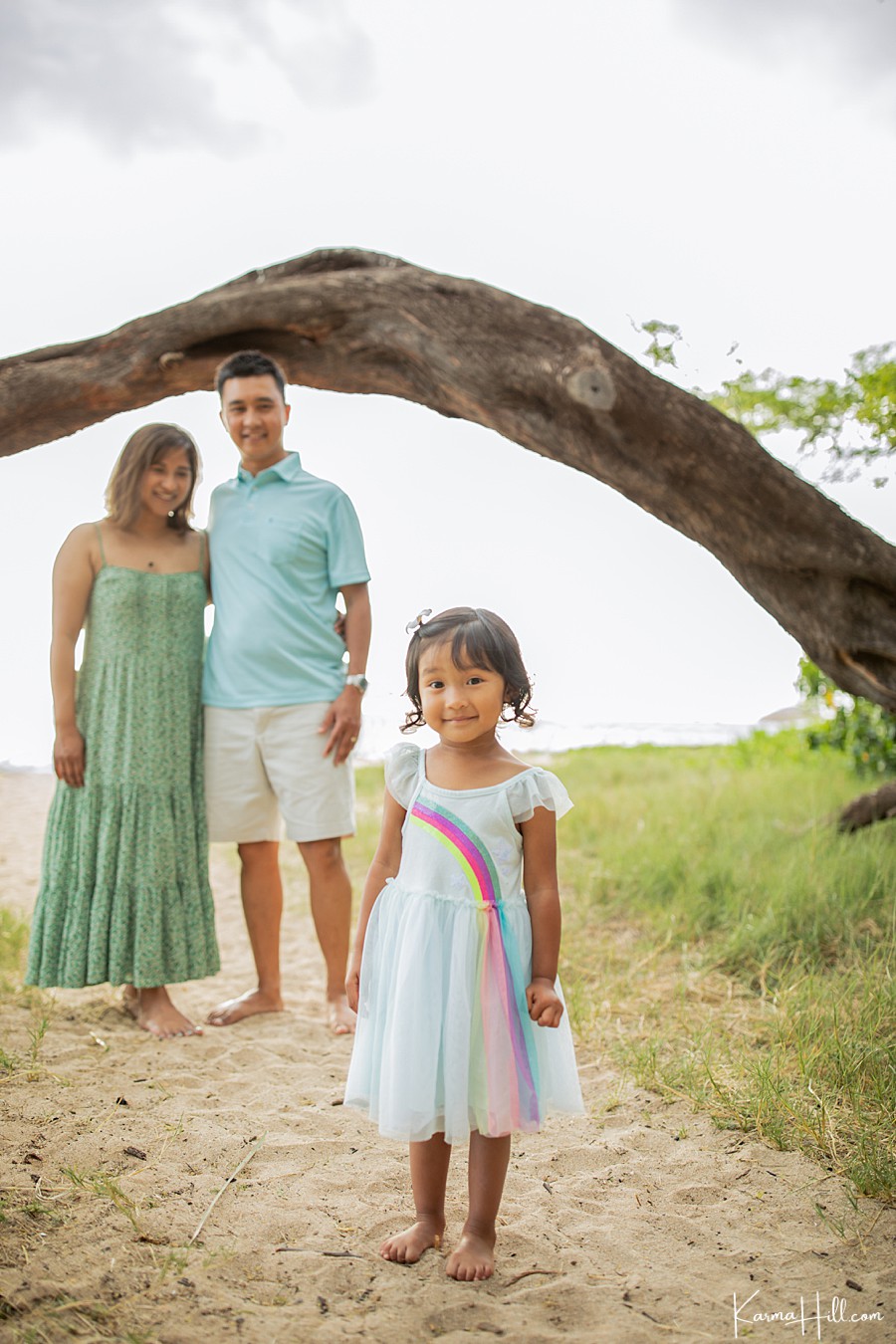 cute photo of a child wearing a rainbow dress with parents on the beach 