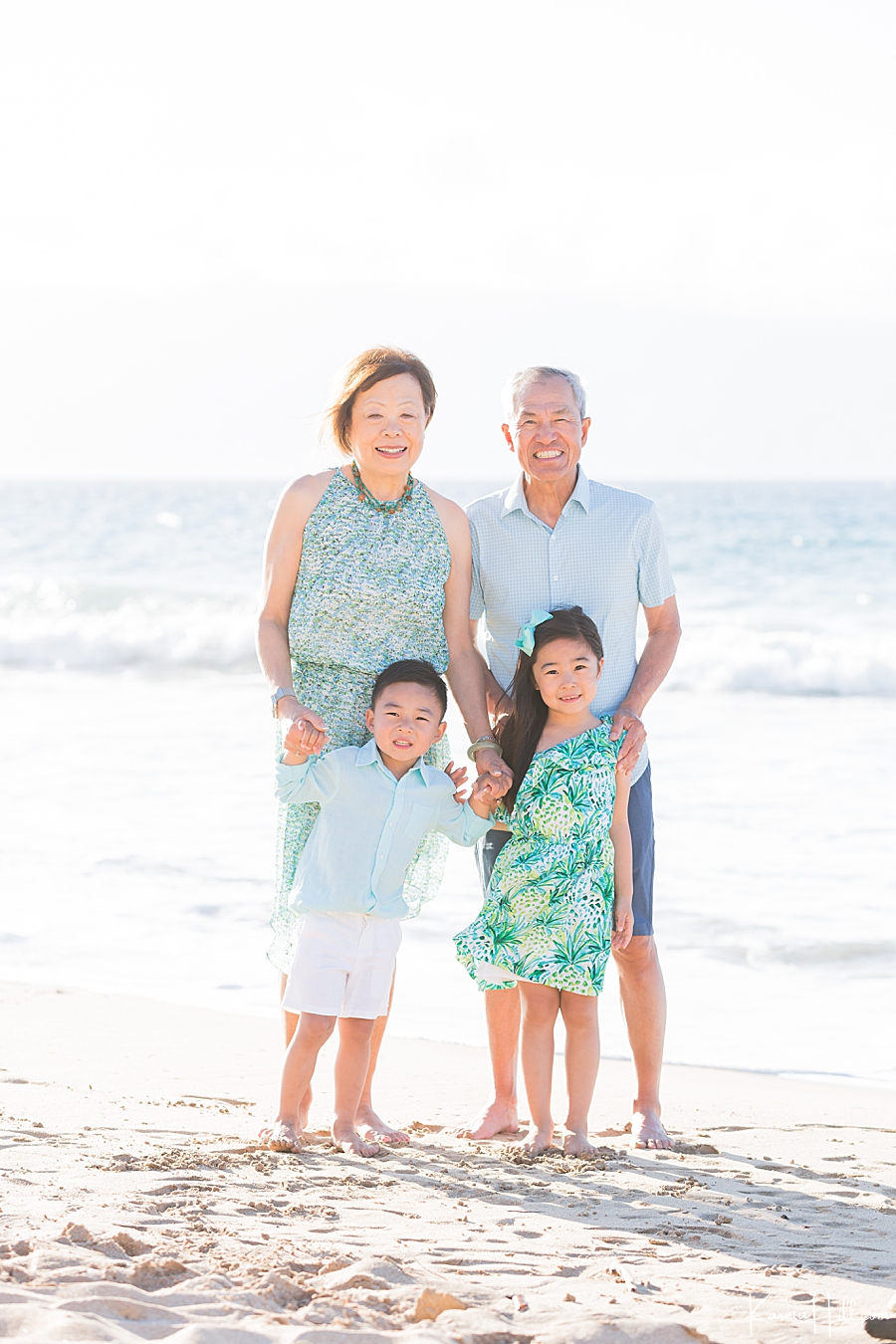 young brother and sister pose with their grandparents on a beach in hawaii 