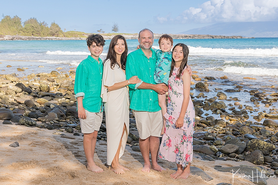 family of five wearing teal and floral pose in front of a rustic hawaiian beach 