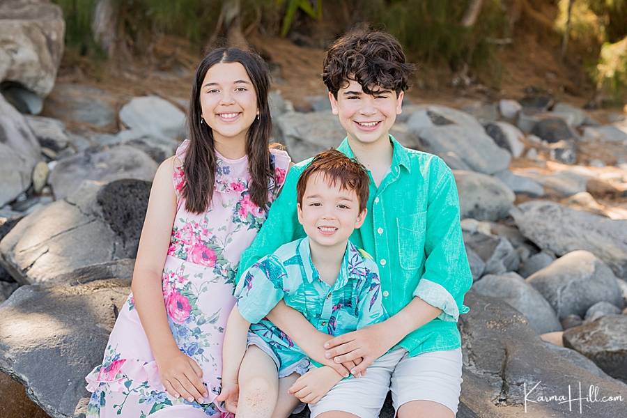 siblings with dark hair smile for family photos on a maui beach 