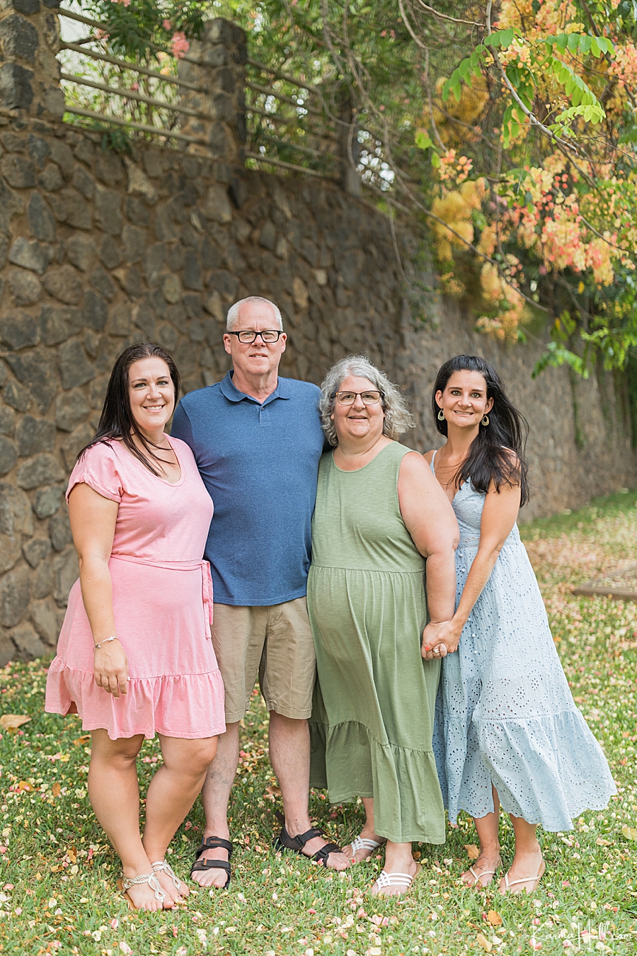 family wearing pastels stands in front of a rock wall in hawaii 