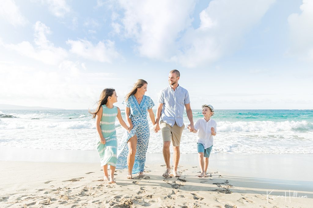 beautiful family of four smile while holding hands and walking on tropical beach 
