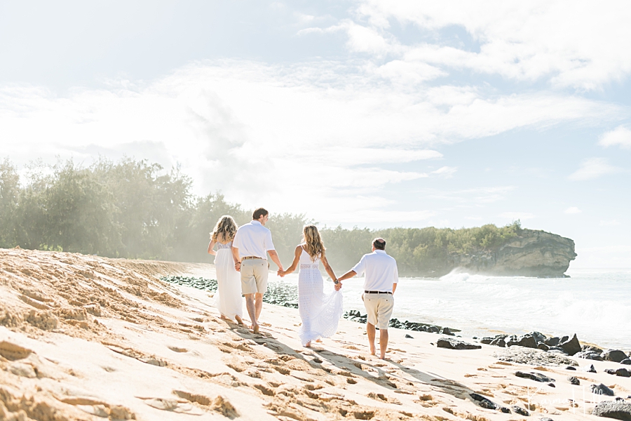 family holds hands as they walk on a hawaii beach with their backs to the camera 