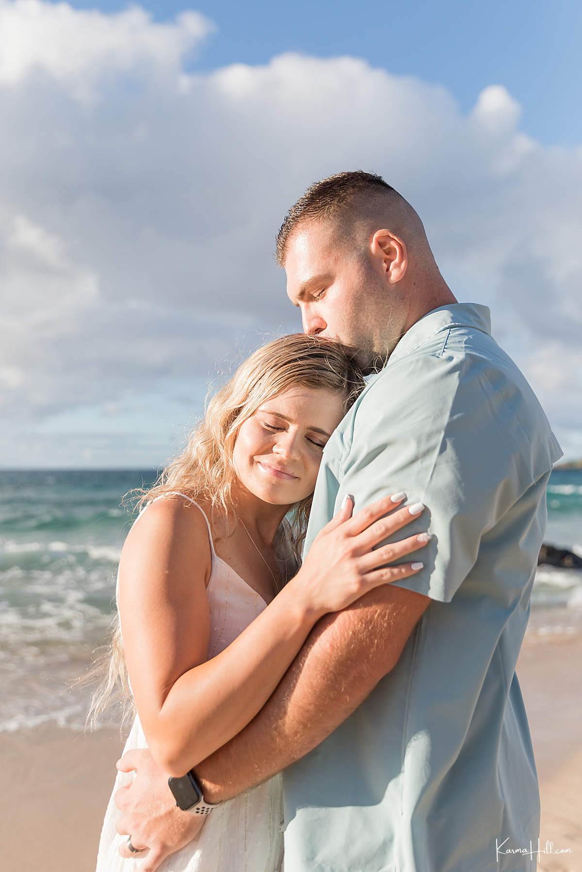 man kisses woman on the head in front of hawaiian ocean 