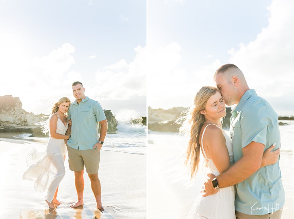 man in blue button down embraces woman in white dress on hawaii beach 