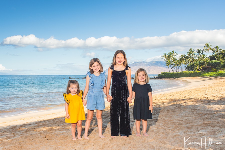 four young sisters with blonde hair stand on maui beach 