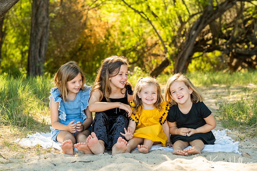 four young sisters laugh and smile on a blanket at the beach 
