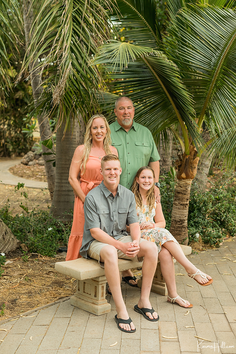 happy family with son and daughter sit on bench in front of palm trees 